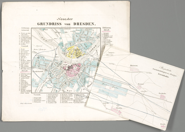Alte Karte von Dresden, Deutschland, mit zwei Papieren im Vordergrund und einem grauen Hintergrund, die detaillierte Straßen, Gebäude und Sehenswürdigkeiten zeigt.