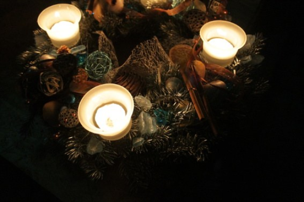 Adventskranz mit brennenden Kerzen, festlicher Schmuck und Lichter auf einem Tisch.