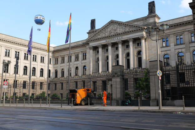 Großes modernes Gebäude mit vielen Fenstern, der Deutsche Bundestag in Berlin, umgeben von Straßeninfrastruktur, Fußgängern und Bäumen unter einem bewölkten Himmel.