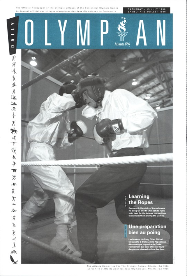 Zwei Boxer in einem Boxring mit Helmen und Handschuhen, umgeben von Seilen, mit dem Text "Olympian Magazine" oben und unten.