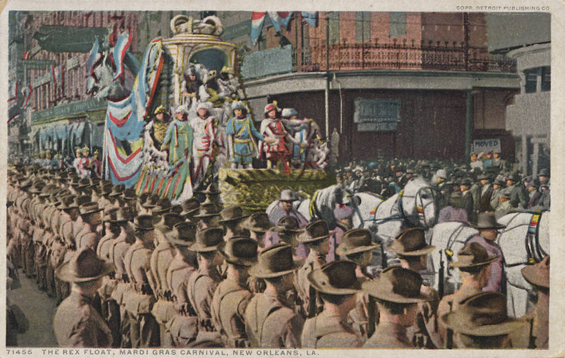 Eine alte Postkarte zeigt einen Mardi-Gras-Umzug in New Orleans mit Menschen zu Pferd, einem geschmückten Festwagen mit Flaggen und Gebäuden im Hintergrund; unten steht 'The Rex Float, Mardi Gras Carnival, New Orleans'.