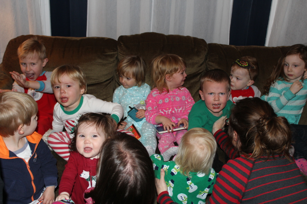 Eine Gruppe von Kindern sitzt auf einem Sofa in einem Raum, jedes hält ein Mobiltelefon, mit einer Frau rechts und einem Vorhang oben im Bild.