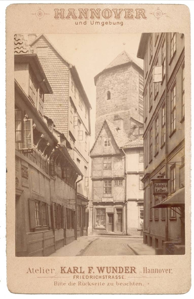 Altes Schwarz-Weiß-Foto einer Straße in Hannover, Deutschland, gesäumt von Gebäuden, mit Text an den oberen und unteren Rändern.