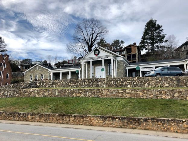 Steinmauer mit parkenden Autos, angrenzende Gebäude mit Fenstern und Türen, Bäume und ein bewölkter Himmel im Hintergrund, als das kürzlich wiedereröffnete Weltkulturerbe-Museum bezeichnet.