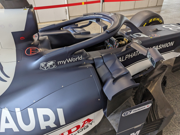 Ein Formel-E-Rennwagen in einem Museum ausgestellt, umgeben von verstreuten Werkzeugen und Materialien, mit einer Wand im Hintergrund.