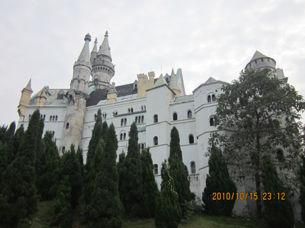 Schloss Neuschwanstein in Deutschland mit weißen Wänden und Fenstern, umgeben von Bäumen und Gras unter einem bewölkten Himmel, mit Text auf der rechten Seite des Bildes.