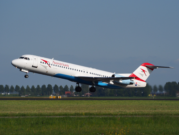 Austrian Airlines Embraer ERJ-190 Flugzeuge starten am Frankfurter Flughafen, mit grünem Gras darunter und Bäumen und Gebäuden im Hintergrund.