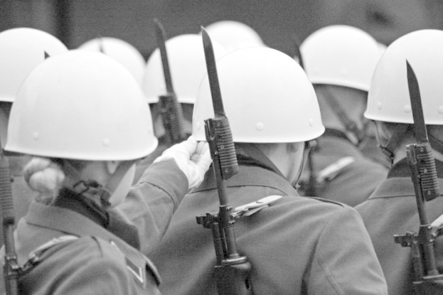 Eine Gruppe von Menschen in Uniformen und Hüten, die Waffen haltend, abgewandt von der Kamera in einem Schwarz-Weiß-Bild.