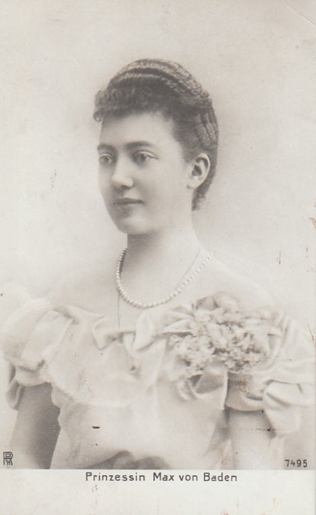 Ein Schwarz-Weiß-Foto von Prinzessin Max von Baden, eine Frau in einem weißen Kleid mit hohem Kragen und langen Ärmeln, deren Haar ordentlich zurückgebunden ist und die mit einem königlichen und würdevollen Ausdruck zur Seite blickt.