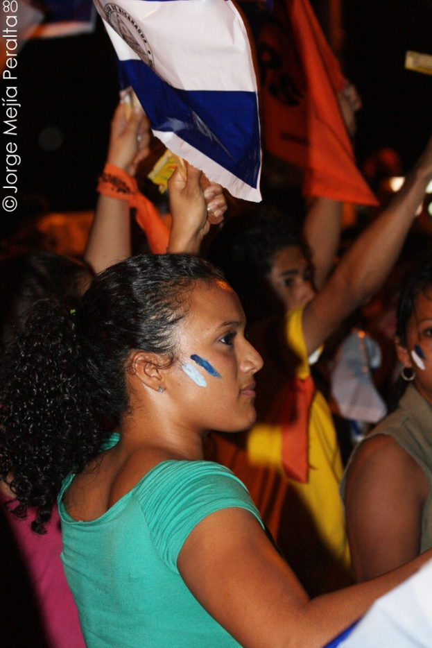 Eine Gruppe von Frauen in grünen T-Shirts, die weißen Stoff halten, während sie auf einer Demonstration stehen, mit weiteren Frauen im Hintergrund.