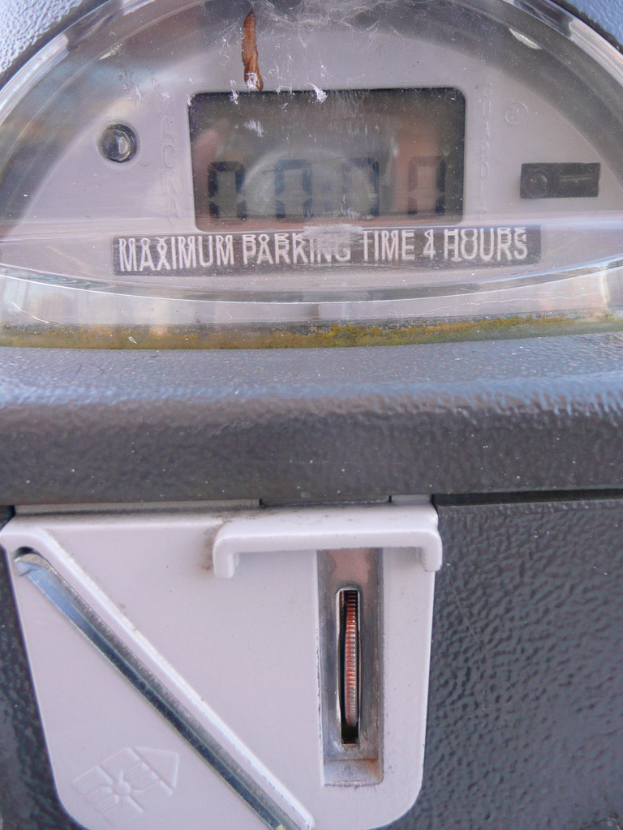 Ein Parkscheinautomat mit der Anzeige "Maximale Parkdauer 4 Stunden" und einem Münzschlitz mit einer Münze.