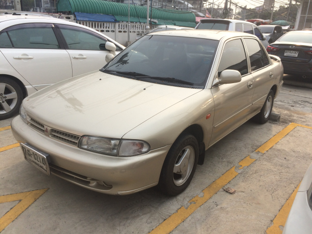 Goldfarbener Wagen auf einem Parkplatz neben anderen Autos geparkt, umgeben von Gebäuden, Polen, Drähten, Bäumen und einem klaren blauen Himmel.