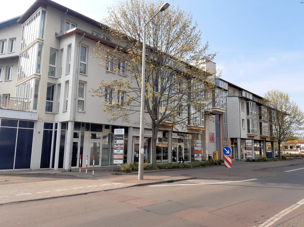 Eine Straßenecke in Stuttgart, Deutschland, mit einem zum Verkauf stehenden Gewerbeobjekt umgeben von Bäumen, Pfählen, Laternen, Schildern, Pflanzen und Fahrzeugen, mit einem bewölkten Himmel im Hintergrund.