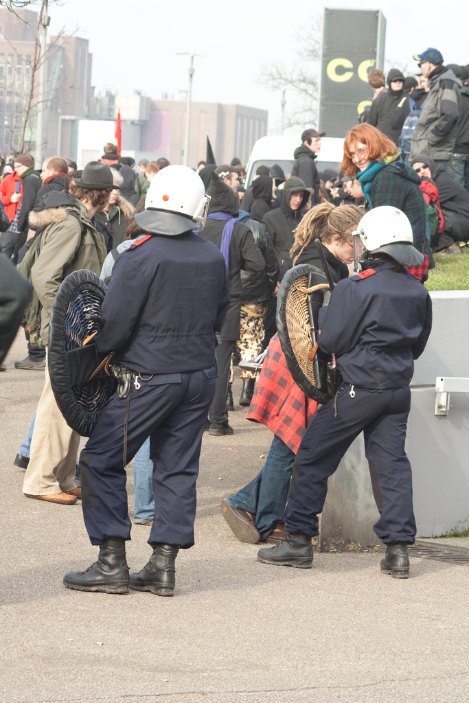 Eine Gruppe von Menschen, die auf der Straße gehen, mit zwei Personen vorne, die wie Polizisten aussehen, Gebäude im Hintergrund und Boden unten.
