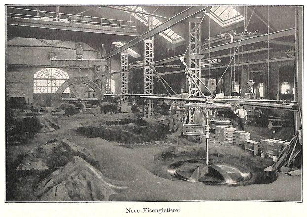 Schwarzes und weißes Foto einer Fabrik mit Arbeitern, die an Maschinen arbeiten, umgeben von Metallstangen und -pfählen, mit der Beschriftung "Neue Eisenglebeerei, die erste Fabrik in Deutschland" unten.