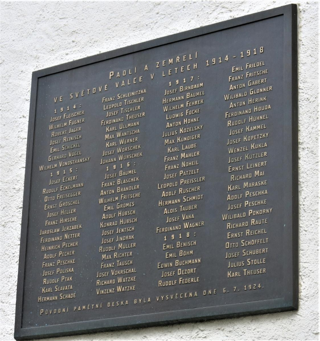 Eine dunkle Metalltafel an einer Gebäudewand mit der Inschrift "Tafel für die Opfer des Holocaust" in fetter Schrift, umgeben von einem dekorativen Rahmen.