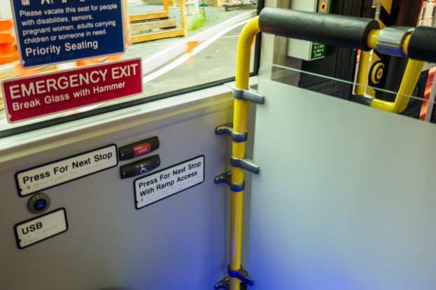 Notausgangsschild an der Seite eines Zuges, mit einer Tür, Griff und Glasfenster, das die Außenlandschaft zeigt.