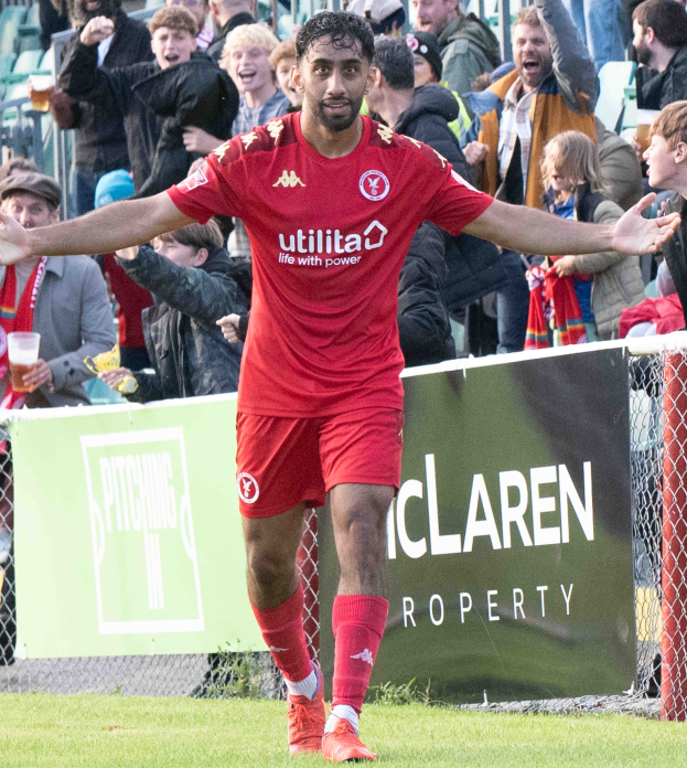 Ein Füßballer in roter Uniform rennt mit ausgebreiteten Armen auf einem Feld, mit einer Menge im Hintergrund und einem Banner mit der Aufschrift "Middlesbrough FC v Swansea City - Sky Bet Championship" im Vordergrund.
