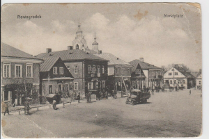 Schwarz-weiß-Fotografie einer Stadtstraße in Nowogrodziec, Deutschland, mit Gebäuden, Menschen, Karren, Pfählen, Bäumen und Himmel, mit der Beschriftung "Marktplatz in Nowogrodeek, Deutschland" oben und unten.