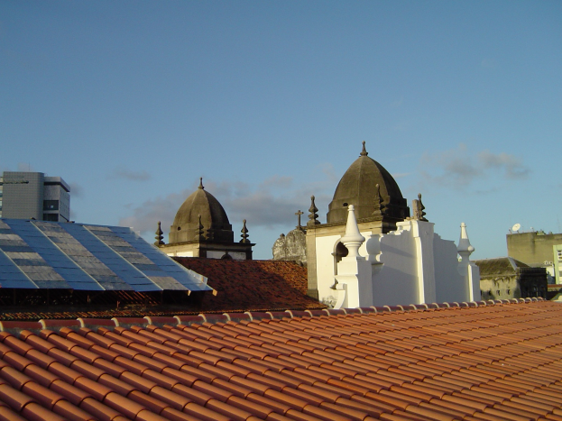 Stadtansicht mit mehreren Gebäuden im Vordergrund, einem blauen Himmel im Hintergrund und Solarpanelen auf einem Dach.