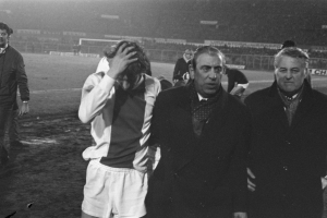 Schwarzes und weißes Bild einer Gruppe von Männern auf einem Fußballfeld mit einem Stadion im Hintergrund, die nach einem Sieg betrübt wirken.