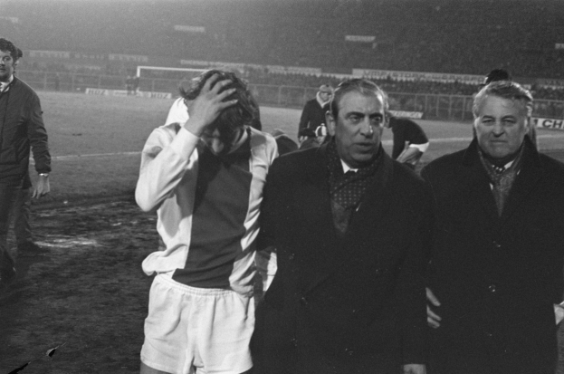 Schwarzes und weißes Bild einer Gruppe von Männern auf einem Fußballfeld mit einem Stadion im Hintergrund, die nach einem Sieg betrübt wirken.