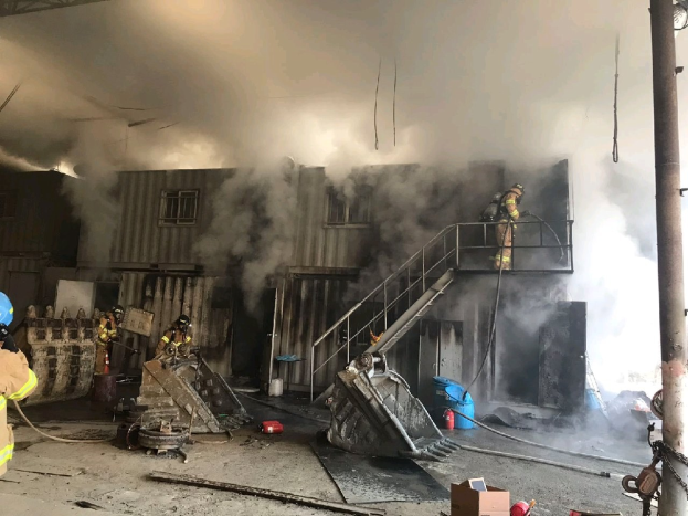 Feuerwehrleute mit Helmen arbeiten daran, ein Lagerfeuer zu löschen, mit Rauch, der aus dem Gebäude aufsteigt und Trümmern, die auf dem Boden verstreut sind.