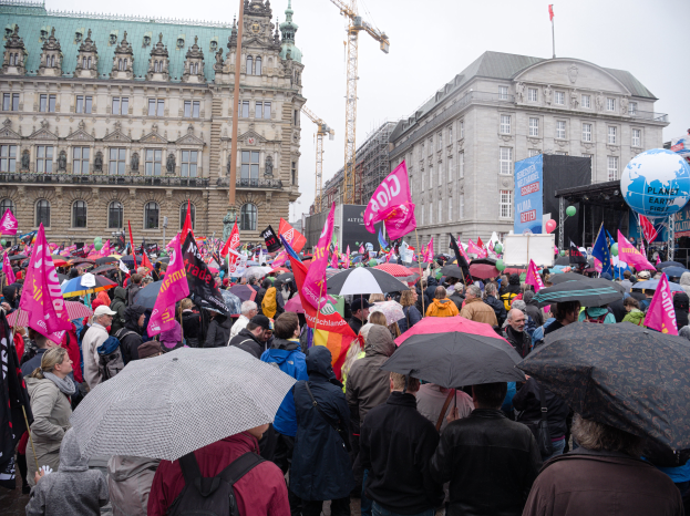 Eine große Gruppe von Menschen mit Schirmen und Transparenten nimmt an einer Frauen-Demonstration in Berlin teil, mit Ballons und Stangen im Vordergrund und dem Himmel im Hintergrund.