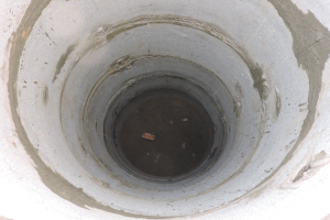 Beton-Abwasserrohr mit mittigem Loch in einer Betonwand und einem Objekt im Loch.