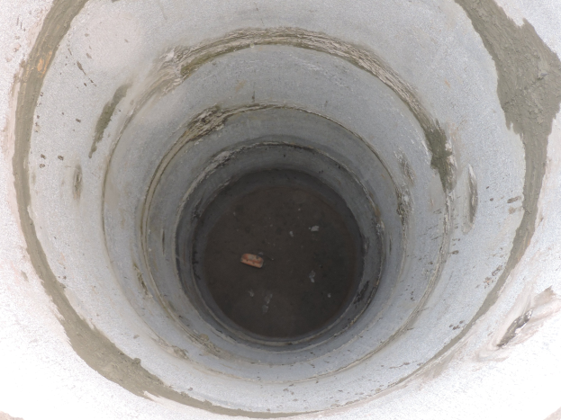 Beton-Abwasserrohr mit mittigem Loch in einer Betonwand und einem Objekt im Loch.