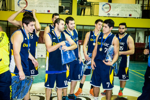 Eine Gruppe von Menschen, einige mit Medaillen und Gegenständen in den Händen, steht vor Bannern und Geländern.