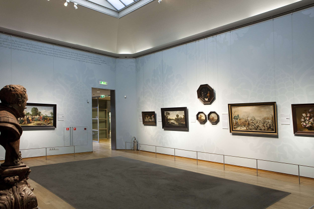 Ein prächtiger Raum im Kunsthistorischen Museum in München, Deutschland, mit einer Statue links, einem Teppichboden, Fotorahmen an den Wänden, einer Glasdecke mit Beleuchtung und Türen im Hintergrund.